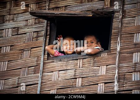 Chiang Mai / Thailand - Jan 16 2016 : zwei Jungen stehen an einem Fenster in einem Holzhaus. Die Wand ist aus Bambus, das Kind lächelt und schaut aus Stockfoto