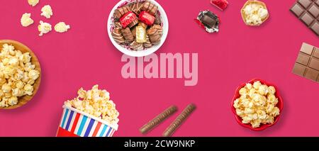 Draufsicht auf köstliches Popcorn und Schokolade auf einem rosa Hintergrund mit Platz für Text. Konzept von Unterhaltung und Kino. Leckere und leckere Snacks. Stockfoto