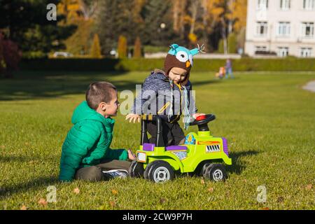 Zwei fröhliche Brüder-Jungen unterschiedlichen Alters haben Spaß beim Spielen mit einem großen Jeep im Rollstuhl auf einem grünen Feld an einem warmen Sommertag. Brüder freundlich Stockfoto