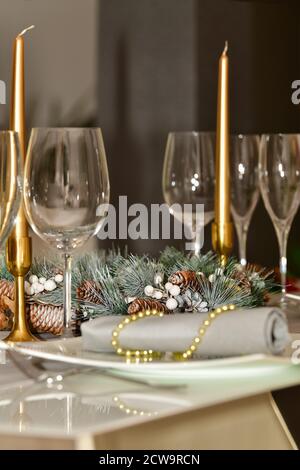 Wählen Sie den Fokus eines Kieferkegelkranzes, umgeben von Gläsern und Kerzen, auf einem Tisch auf einem unfokussieren Hintergrund. Weihnachtsfeiertag und Feier conce Stockfoto