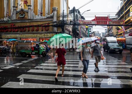 Pendler gehen schnell über die Straße mit Schutzschirmen während eines Regensturms in Bangkoks Chinatown. Stockfoto