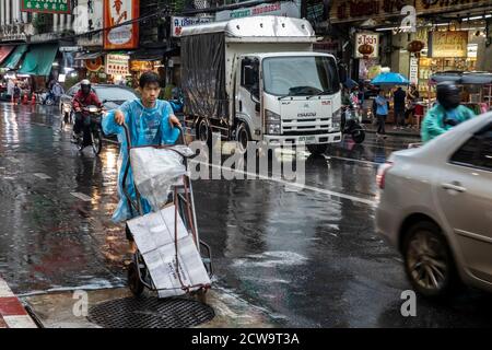 Nach der Lieferung schiebt ein junger Mann seinen leeren Handwagen während eines Regensturms eine große Straße in Bangkoks Chinatown hinunter. Stockfoto