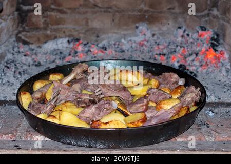 Köstliches gegrilltes Fleisch mit Kartoffeln in der Pfanne auf offener Flamme Stockfoto
