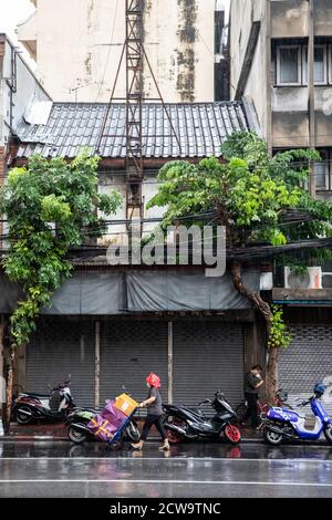 Ein Lieferer schiebt einen mit lila Boxen beladenen Handwagen durch den Regen in Bangkoks Chinatown. Stockfoto