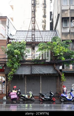 Ein Lieferer schiebt einen mit lila Boxen beladenen Handwagen durch den Regen in Bangkoks Chinatown. Stockfoto