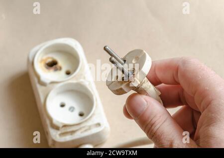 Ein Elektriker demonstriert einen verbrannten Stecker. Weißes Verlängerungskabel nach Kurzschluss in der männlichen Hand. Elektrische Sicherheit. Stockfoto