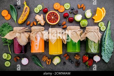 Bunte gesunde Smoothies und Säfte in Flaschen mit frischen tropischen Früchten und Superfoods auf dunklem Stein Hintergrund mit kopieren. Stockfoto