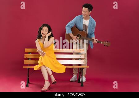Gitarre spielen im jungen Mann und hören Die Musik junger Frauen Stockfoto