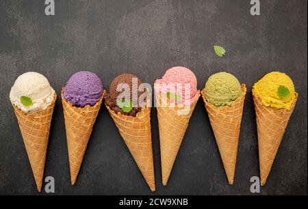 Verschiedene Eis Geschmack in Zapfen Heidelbeere, Pistazie, Mandel, Orange und Schokolade Setup auf dunklen Stein Hintergrund. Sommer und Süße Menükonzept Stockfoto