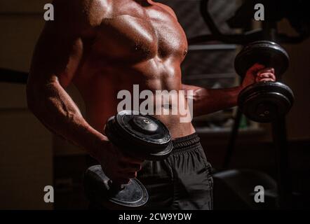 Muskulöser Mann auf Turnhalle Hintergrund mit Hantel. Athlet im Fitnesstraining mit Hanteln. ABS und Bizeps. Muskulöser Mann mit Hantel. Stark Stockfoto