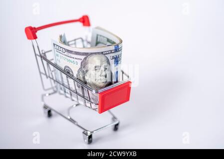 Der Wagen aus dem Supermarkt ist mit Geld gefüllt. Dollar in einem Einkaufswagen auf weißem Hintergrund. Das Konzept des Shoppings. Stockfoto
