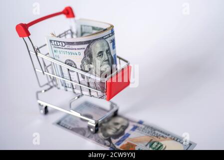 Der Wagen aus dem Supermarkt ist mit Geld gefüllt. Dollar in einem Einkaufswagen auf weißem Hintergrund. Das Konzept des Shoppings. Stockfoto