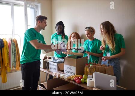 Diverse Freiwillige packen, sammeln humanitäre Hilfe in Spendenbox. Multi-ethnische Gruppe von Menschen in karitativen Stiftung in Krisen und Obdachlosen helfen Stockfoto