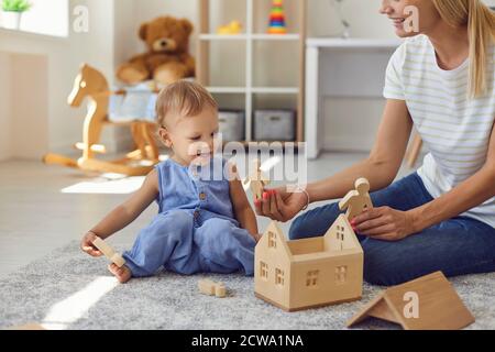 Fröhliche junge Kindermädchen und kleines Kind spielen mit Holzblöcken Im gemütlichen Kinderzimmer Stockfoto