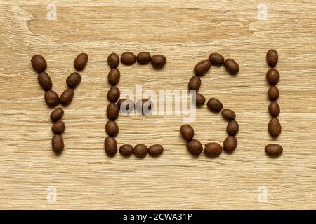 Das Wort 'Ja' wurde mit gerösteten arabica-Kaffeebohnen auf einem Holztisch ausgelegt. Stockfoto