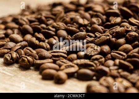 Geröstete arabica-Kaffeebohnen, in loser Schüttung auf einem Holztisch. Stockfoto