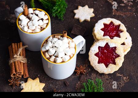 Zwei Tassen heiße Schokolade oder Kakao mit Marshmallow und Zimtstange, Bitterschokolade, Wintergewürzen und Marmelade füllenden Keksen. Festliche Weihnachten oder Stockfoto