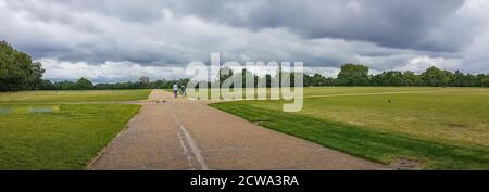 Panorama des Hyde Park Field mit zwei unkenntlichen Menschen, die mitten drin spazieren. Wolkiger Himmel als Hintergrund. Stockfoto