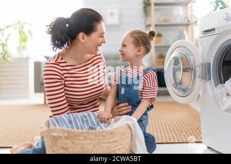 Schöne junge Frau und Kind Mädchen kleinen Helfer haben Spaß und Lächeln, während die Wäsche zu Hause. Stockfoto