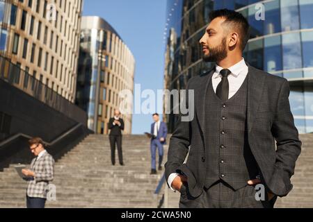 Junge elegante Geschäftsmann in Anzug suchen weg mit nachdenklichen Look Während Sie in der Stadt stehen Stockfoto