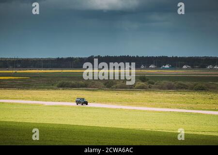 SUV-Auto bewegt sich auf Landstraße auf dem Hintergrund von Grün Frühlingsfelder Oder Wiese Im Sonnigen Tag Stockfoto