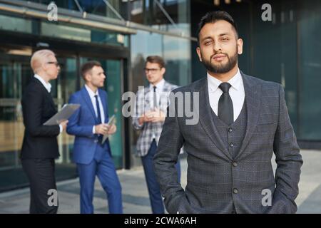 Porträt des jungen Führers in eleganten Anzug Blick auf die Kamera Im Freien mit seinem Team im Hintergrund Stockfoto