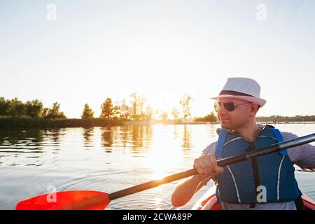 Junger Mann im Hut paddelt mit dem Kajak auf dem Fluss Oder See Stockfoto