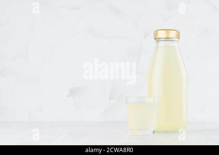 Frischer gelber Ananassaft in Glasflasche Nachbau mit Weinglas auf weißem Holztisch im hellen Innenraum, Schablone für Verpackung, Werbung, Design Stockfoto