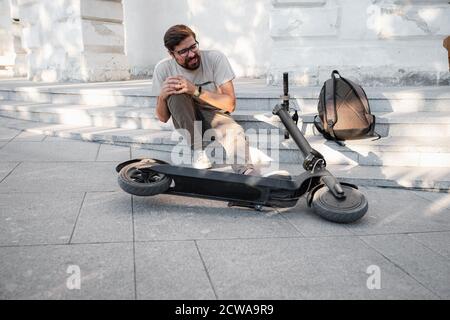 Junger Mann Unfall Mit Einem Elektroroller Auf Der Straße. Ein Mann fiel von einem Roller auf einer Stadtstraße. Stockfoto