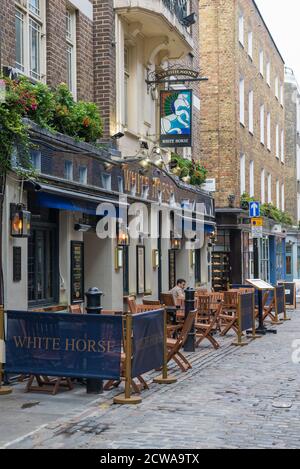 Ein einsitzender Mann, der vor dem White Horse Pub in der Newburgh Street, Soho, London, England, UK, an einem Pflastertisch sitzt Stockfoto