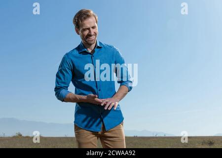 Wunderschöner, legerer Mann mit blauem Hemd und reibenden Händen, während er mit blauem Himmel glücklich nach draußen blickt Stockfoto