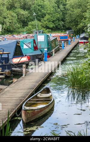 Narrowboats und ein altes Kanu, das an einer Boadwalk in Welford Marina, Grand Union Canal, Northamptonshire, England festgemacht ist. Stockfoto