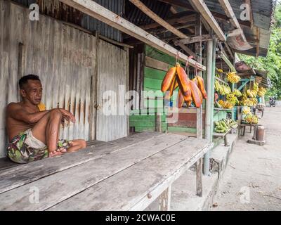 Ambon Island, Indonesien - 11. Februar 2018: Ein Mann verkauft eine riesige Orangenbanane. Bananen hängen an einem Marktstand in einer kleinen Stadt auf der Insel Ambon, Stockfoto