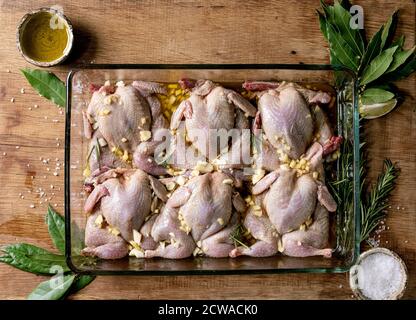 Rohe, unbehaarte Wachteln Schmetterling in Marinade in Glasbackblech mit Kalk, Salz, Pfeffer, Olivenöl, Knoblauch und Grüns über Holzschneidebrett. Flach l Stockfoto