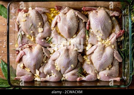 Rohe, unbehaarte Wachteln Schmetterling in Marinade in Glasbackblech mit Kalk, Salz, Pfeffer, Olivenöl, Knoblauch und Grüns über Holzschneidebrett. Flach l Stockfoto