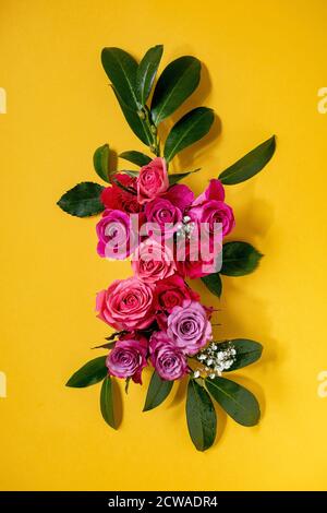 Kreatives Layout mit schönen rosa Rosen Blumen und grünen Blättern auf hellgelbem Hintergrund. Flaches Lay. Grußkartenkonzept Stockfoto