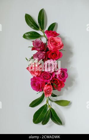 Kreatives Layout mit schönen rosa Rosen Blumen und grünen Blättern auf grauem Hintergrund. Flaches Lay. Grußkartenkonzept Stockfoto