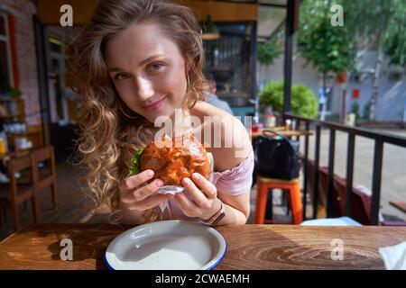 Schöne kaukasische Frau essen einen leckeren Burger an sonnigen Tag Stockfoto