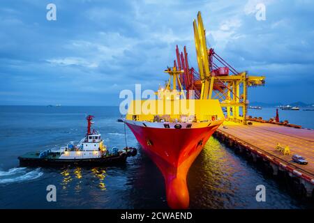 Schlepper schieben große Frachtschiff zu Liegeplatz am Hafenterminal. Hafenterminalbetrieb und Umschlagausrüstung. Stockfoto