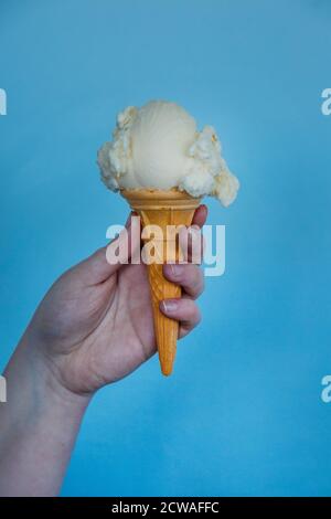 Hand hält eine Kugel Eis in einem Kegel Mit blauem Hintergrund Stockfoto