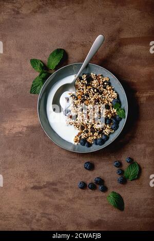 Hausgemachte knackige gebuffte Hirsekorngranola mit getrockneten Früchten und Nüssen in Keramikschale, mit Joghurt, Minze und Zutaten oben. Braune Textur Backgr Stockfoto