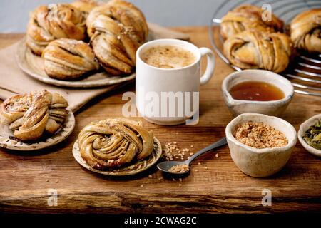 Traditionelle schwedische Kardamom süßen Brötchen Kanelbulle auf Kühlregal, Zutaten in Keramik-Schüssel oben, Tasse Kaffee auf Holztisch. Stockfoto