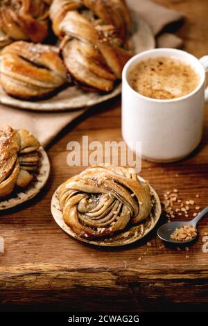 Traditionelle schwedische Kardamom süßen Brötchen Kanelbulle auf Kühlregal, Zutaten in Keramik-Schüssel oben, Tasse Kaffee auf Holztisch. Stockfoto