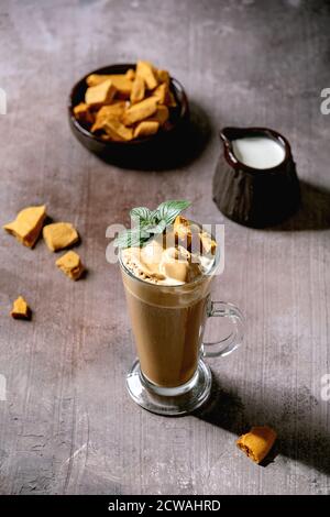 Dalgona schaumig Kaffee Trend koreanisch Getränk Latte Espresso mit Kaffee Schaum in hohen Glas, dekoriert von Dalgona Zinken Toffee Süßigkeiten und Minze. Grau konkar Stockfoto