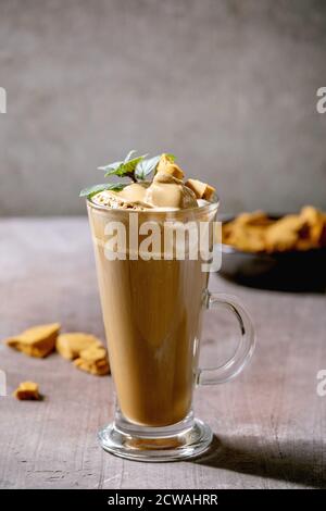 Dalgona schaumig Kaffee Trend koreanisch Getränk Latte Espresso mit Kaffee Schaum in hohen Glas, dekoriert von Dalgona Zinken Toffee Süßigkeiten und Minze. Grau konkar Stockfoto
