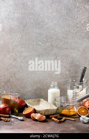 Zutaten für das Backen zu Hause. Mehl, Eier, Rohrzucker, Milch in verschiedenen Schüsseln, Blutorangen und Gewürze. Hintergrund mit grauer Textur Stockfoto