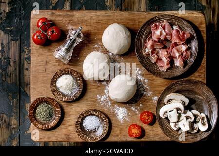 Teig für Pizza napolitana Kochen. Drei Kugeln aus frischem, selbstgemachtem Weizenteig, Prosciutto und Zutaten in Keramikplatten oben auf Holztisch. Hom Stockfoto