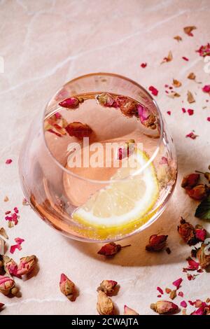 Cocktailgläser aus rosa Rosenchampagner, Apfelwein oder Limonade mit trockenen Rosenblüten und Zitrone. Hintergrund aus rosa Marmor. Nahaufnahme Stockfoto