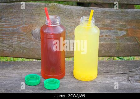 Orangen- und Fruchtlimonade in Flaschen mit Stroh auf Holzterrasse. Minimalismus im Sommer. Stockfoto