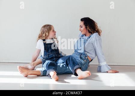 Mama Brünette und Tochter blond in Jeans sitzen auf die Boden Stockfoto
